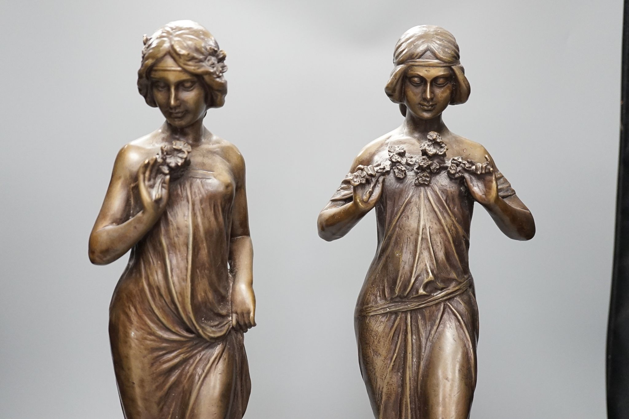 After Jean-Antoine Houdon, (French 1741-1828), a pair of bronze figures of lady’s holding flowers, on marble bases, 52cm